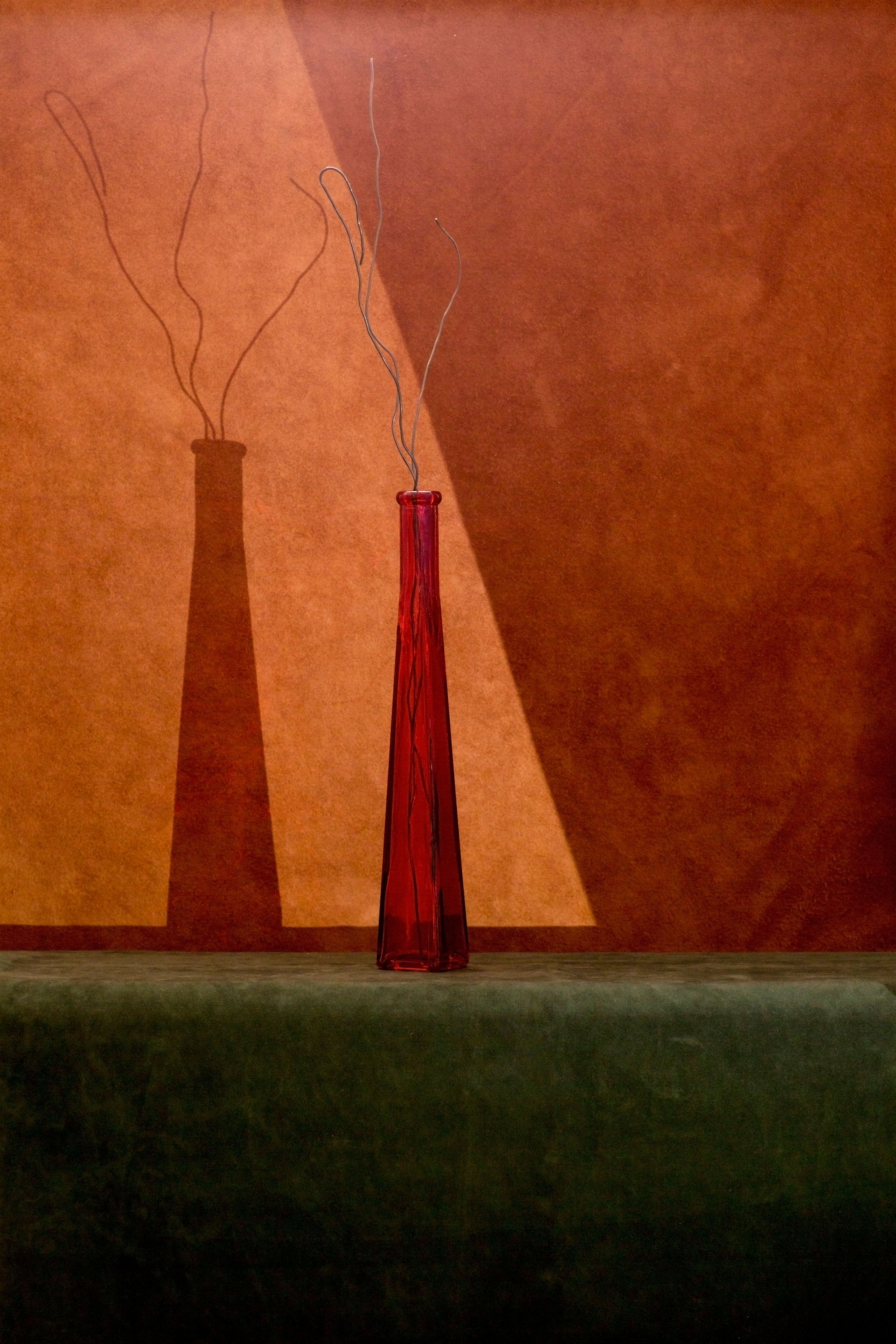 A red-toned still life with a drinking glass and strong afternoon shadows.