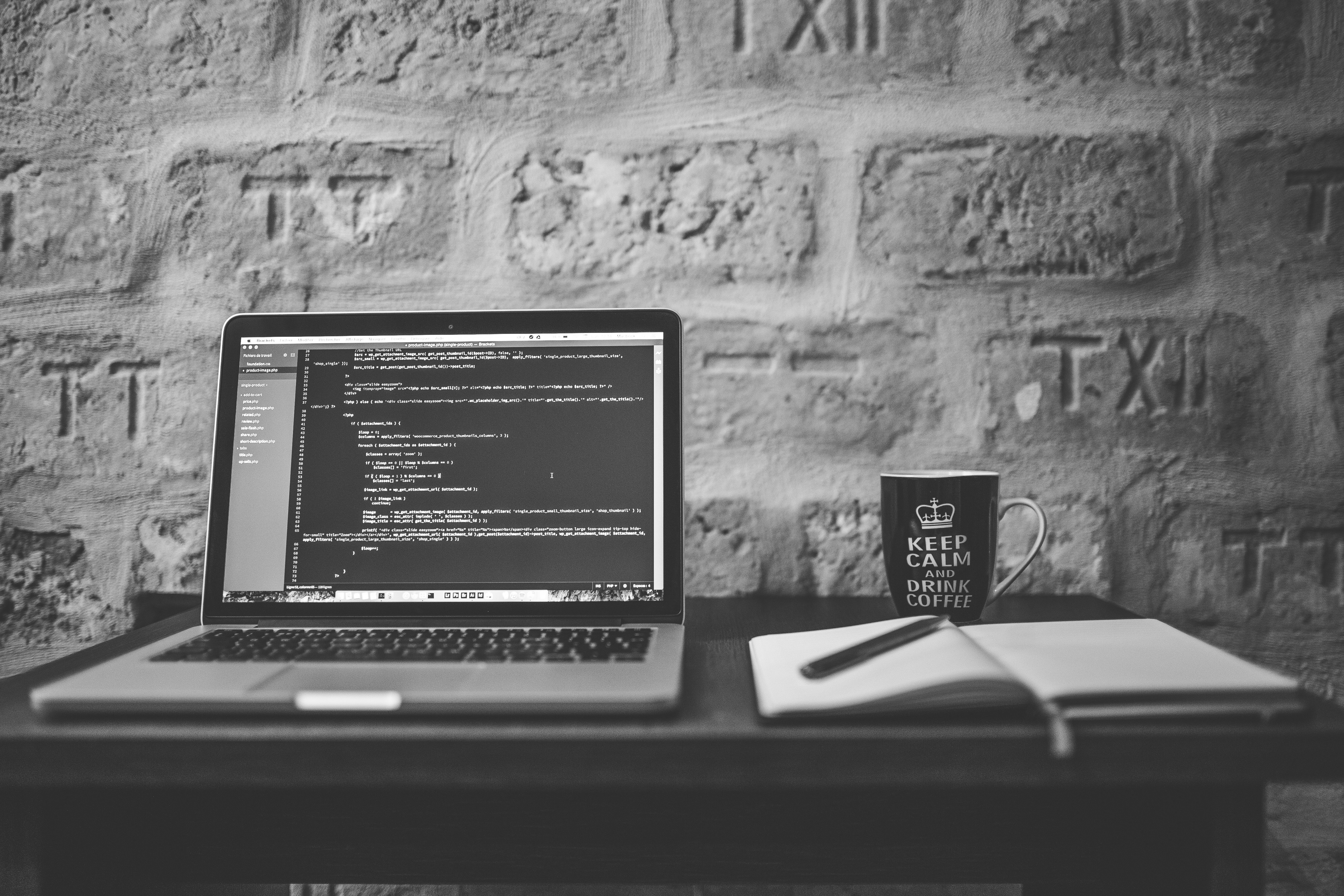Open laptop beside a notebook and a cup of coffee on a desk.
