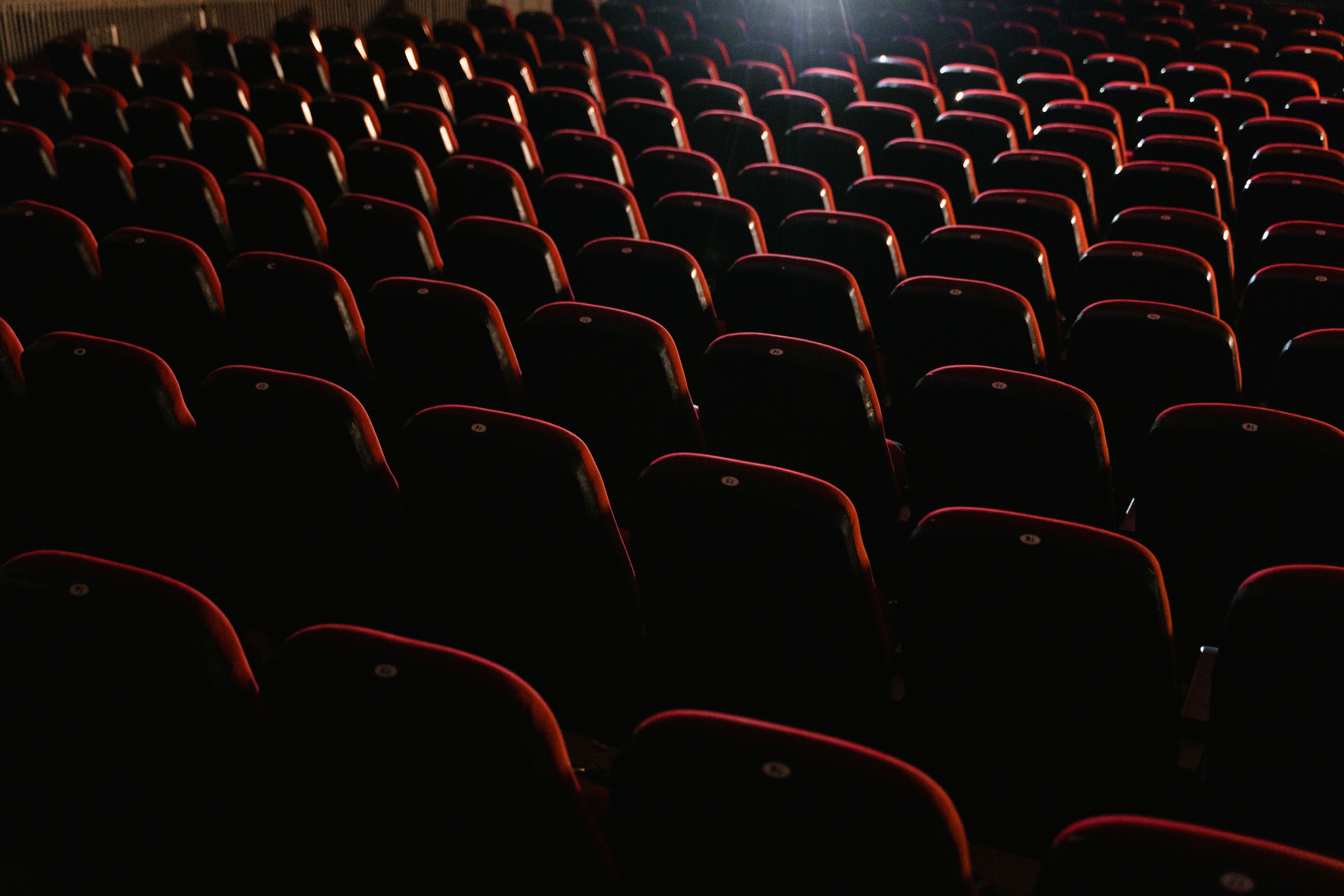 Rows of empty red seats facing an illuminated theatre stage.